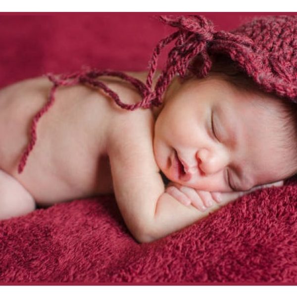 Newborn girl wears a red crochet hat while sleeping in the bed with a red background. Selective Focus